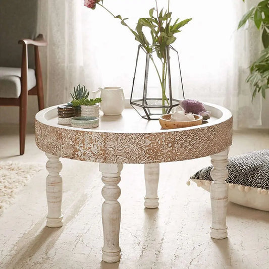 A white round coffee table with a floral pattern on the tabletop and four wooden legs.