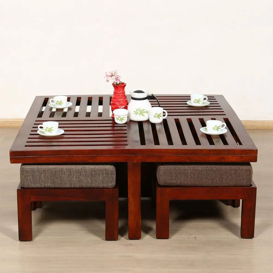 A square coffee table made of sheesham wood with slatted design, accompanied by four upholstered stools.