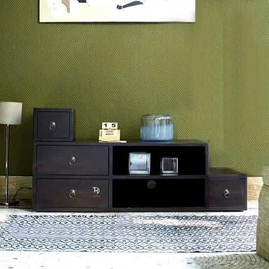 A brown Night Wind TV Cabinet with four drawers and two open shelves, placed against a green wall on a patterned rug.
