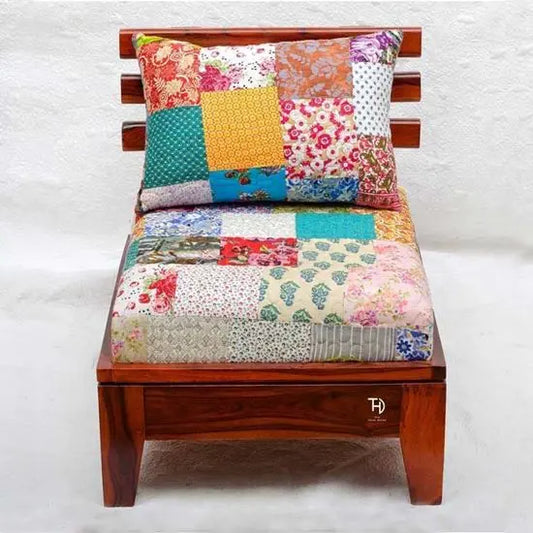 A single-seater sofa with a honey finish wooden frame and multicolored cotton patch fabric upholstery, accompanied by a multicolored cushion.