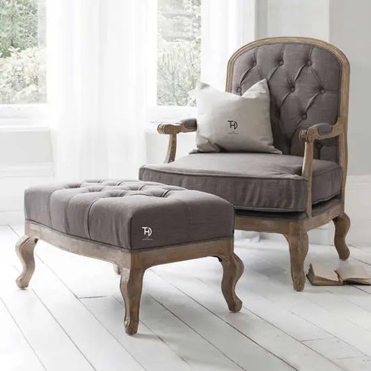 An elegant gray upholstered chair with tufted backrest and seat, accompanied by a matching footstool.