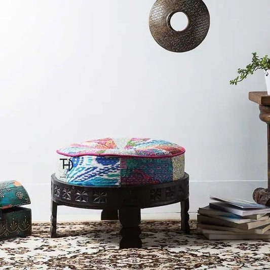 A round footstool made of sheesham wood with a multicolored fabric cushion on top.