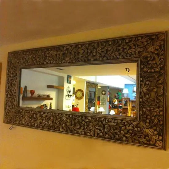 A hand-carved wooden mirror frame with floral patterns, displayed on a wall.