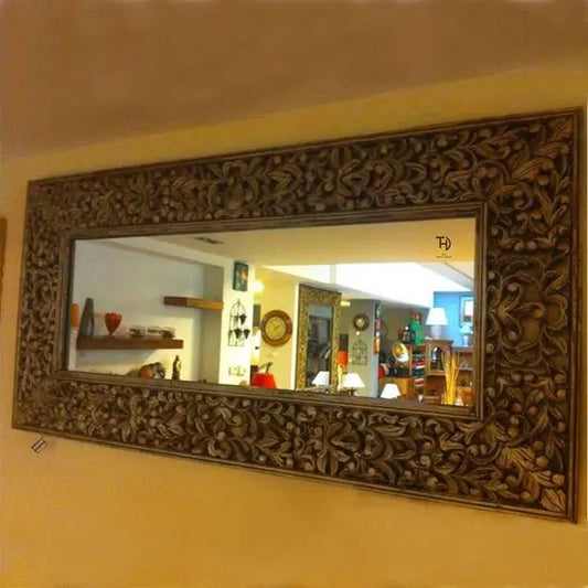 A hand-carved wooden mirror frame with floral patterns, displayed on a wall.