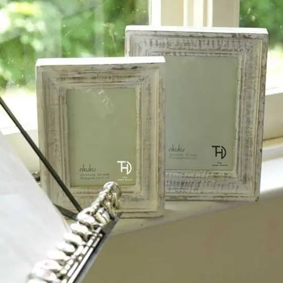 Two wooden photo frames with a rustic white finish on a windowsill, with one slightly in front of the other.