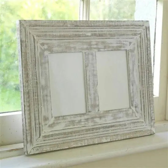 A rustic white photo frame made of mango wood with a distressed finish, designed to hold two photos, placed on a windowsill.