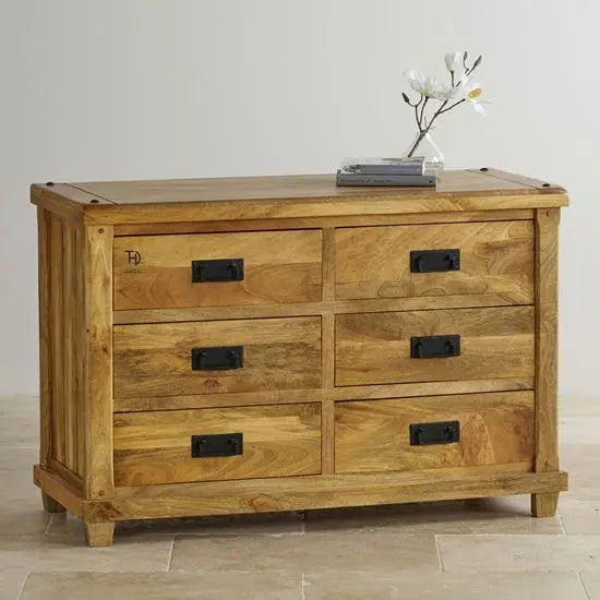 A Devi Chest of 6 drawers made from mango wood with black handles, featuring a solid brown color and a contemporary design.