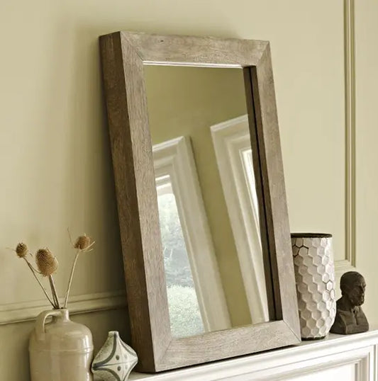 A rectangular Devi solid wood mirror frame in a natural wood color, displayed in an interior setting with a mirror reflection.