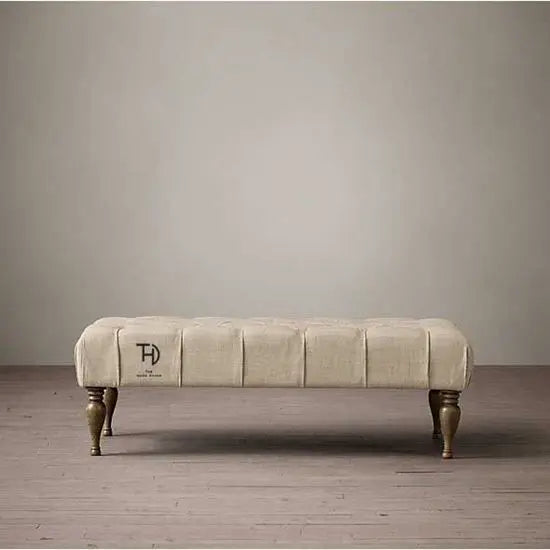 An upholstered cream fabric coffee table with tufted design and bottle-shaped turned wooden legs.