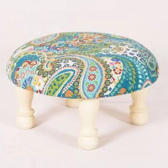 A round low stool with dome legs covered in a blue fabric with a floral and paisley pattern.