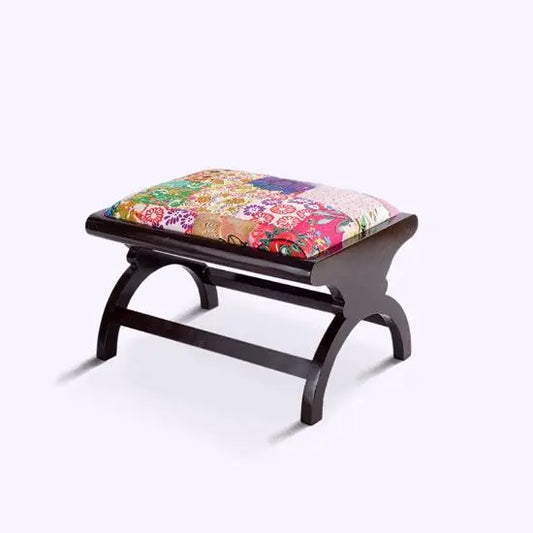 A wooden footstool with a multicolored patchwork fabric cushion on top.