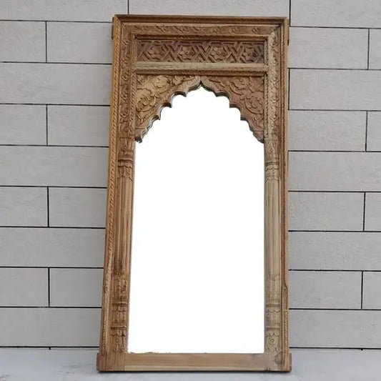 An ornate wooden mirror frame with carved details, standing against a white brick wall.