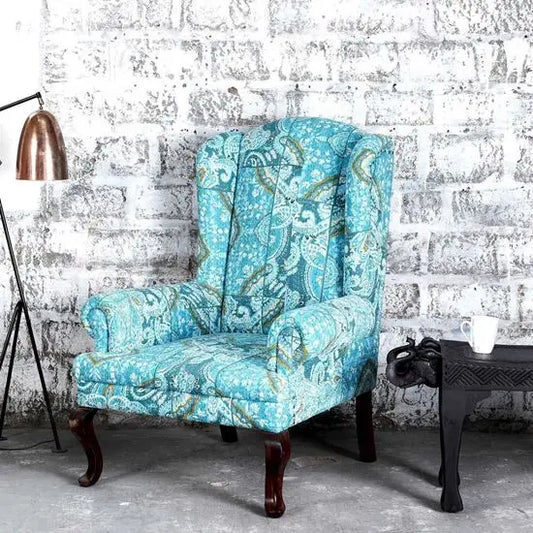 A blue upholstered wing chair with handcrafted katha pejali fabric and wooden legs.