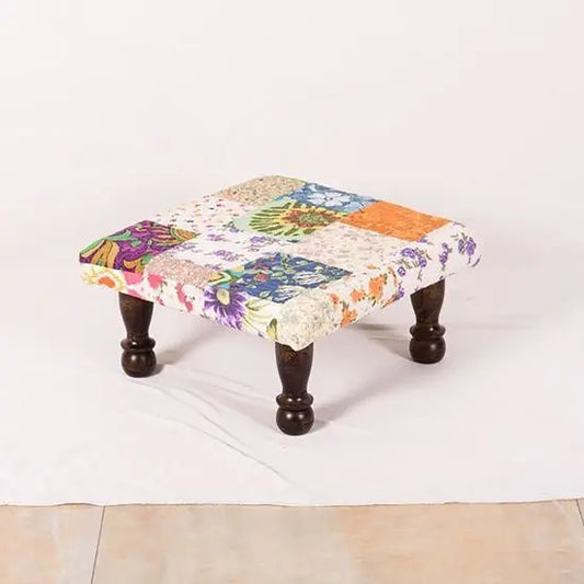 A square-shaped Patchwork Chowki with multicolored floral and geometric patterned fabric on top, supported by four wooden legs.
