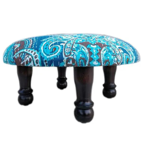 A round upholstered stool with paisley pattern fabric on top.