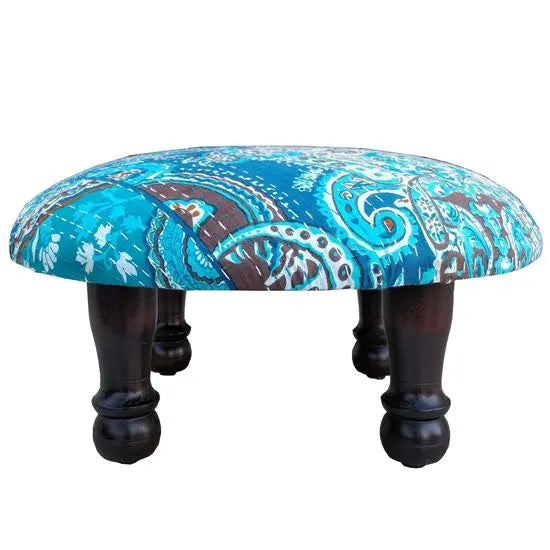 A round upholstered stool with a blue and brown paisley pattern fabric on top and dark wooden legs.