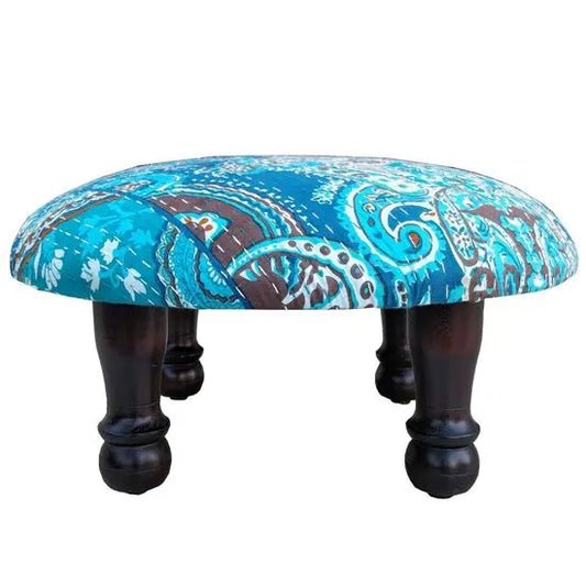A round upholstered stool with a blue and brown paisley pattern fabric on top and dark wooden legs.