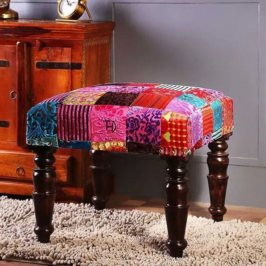 A multicolored patchwork fabric covered stool with dark wooden legs.