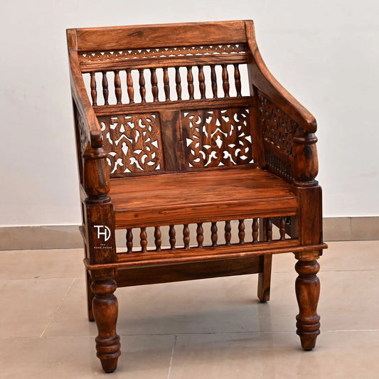 A wooden chair with intricate carvings and a honey-colored finish, featuring a spindle back design and ornate armrests.