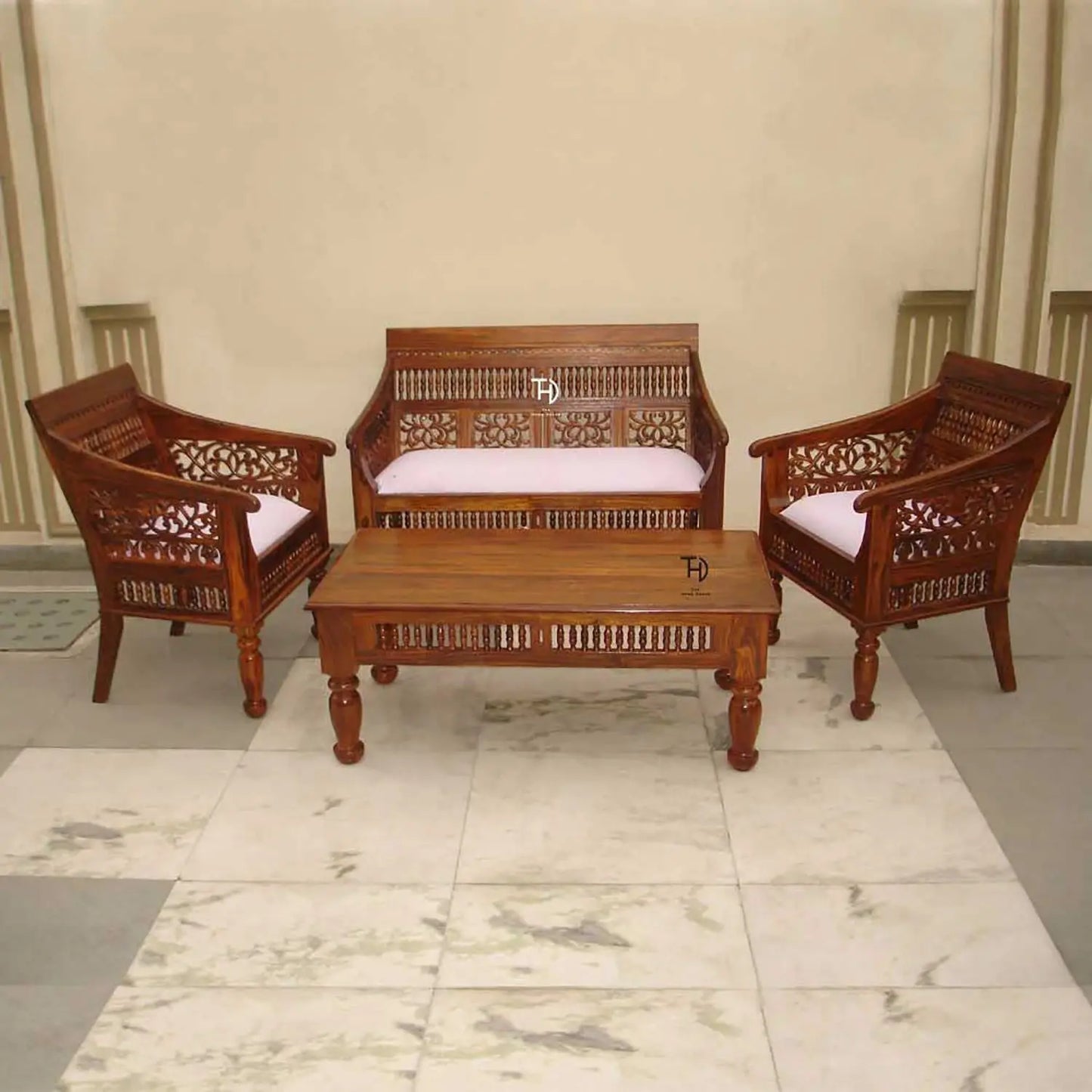 A vintage sofa set made of wood with intricate carvings, featuring two armchairs and a matching coffee table, all with white cushions.