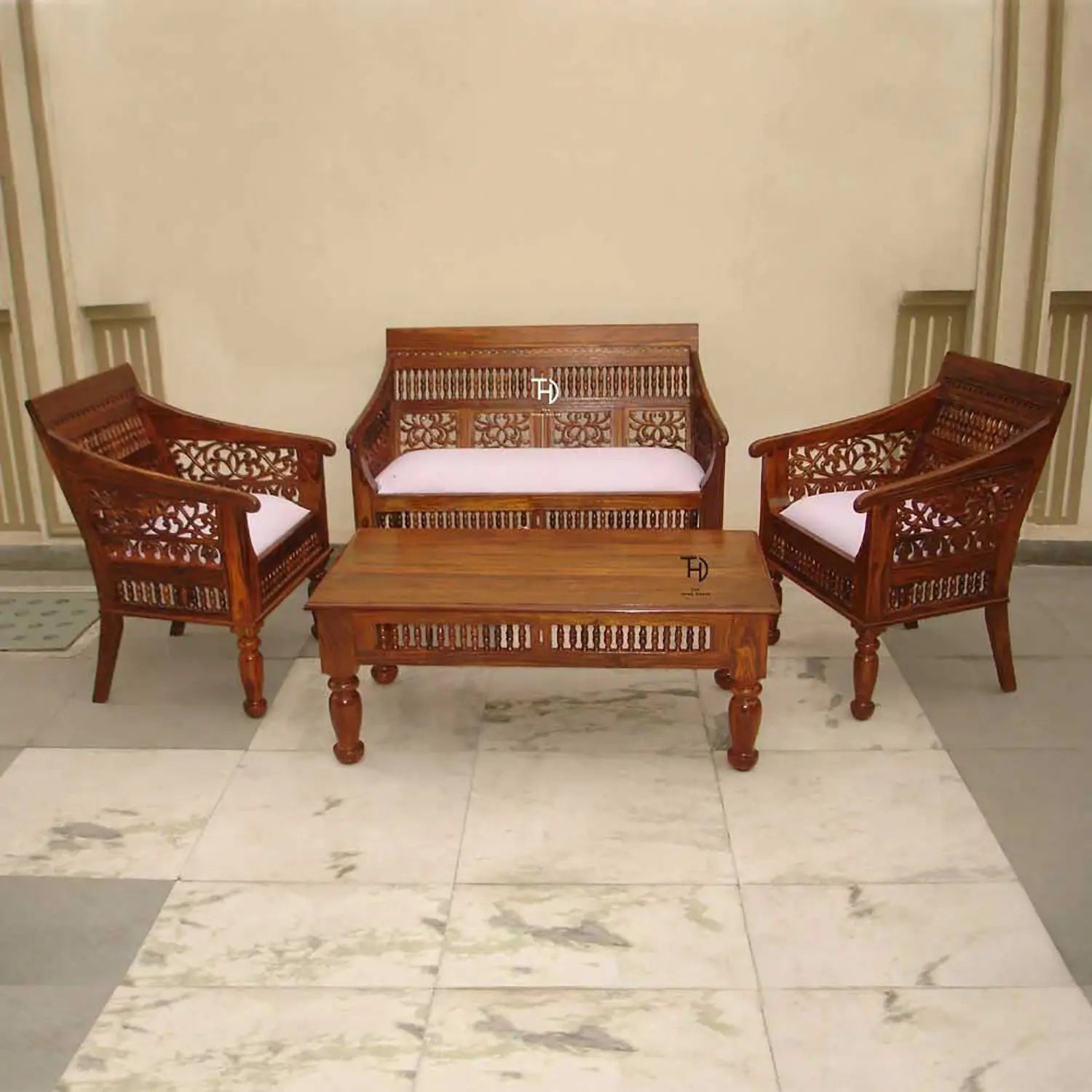 A vintage sofa set made of wood with intricate carvings, featuring two armchairs and a matching coffee table, all with white cushions.