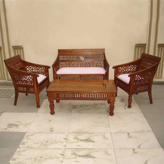 A vintage sofa set made of wood with intricate carvings, featuring two armchairs and a matching coffee table, all with white cushions.
