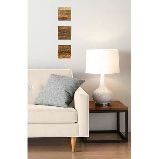 A set of three wooden decorative wall arts displayed above a sofa cushion, with a lamp and a picture frame in the setup.