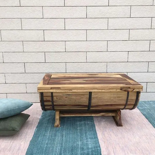 A barrel-shaped coffee table made of Sheesham wood with metal strips on the sides.