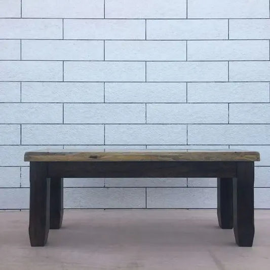 A two-seater dining bench made of mango wood with a two-tone finish, placed against a white tiled wall.