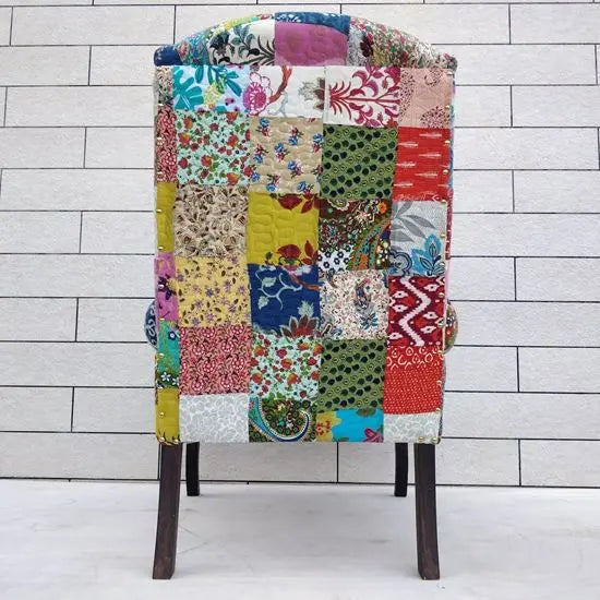 A wing chair with multicolored assorted cotton patch fabric on its backrest and seat.