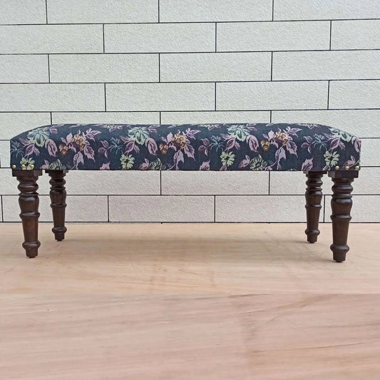 An upholstered bench with a floral pattern on a dark background, featuring wooden legs.