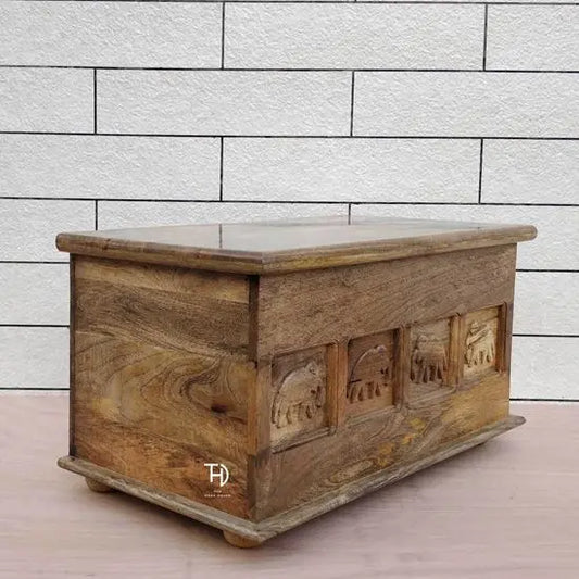 A rectangular mango wood trunk coffee table with elephant carvings on the front.