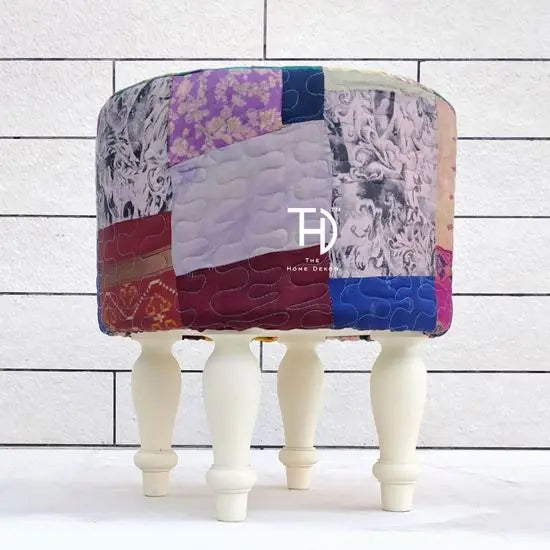 A multicolored patchwork pouf with silk upholstery on a Sheesham wood structure, with white-painted legs.
