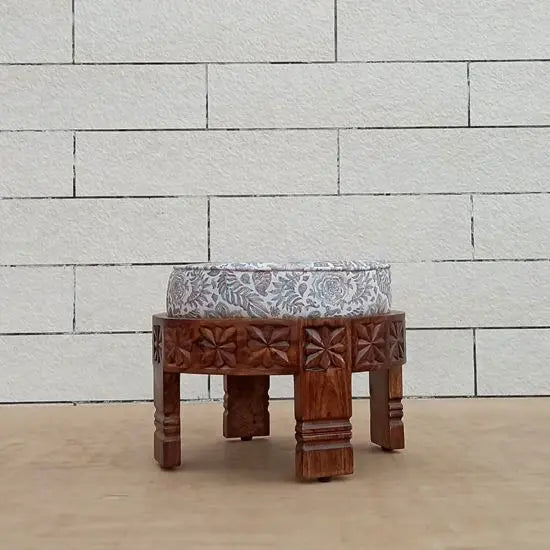 A hand-carved cream-colored footstool made from Sheesham wood with a block print fabric top.