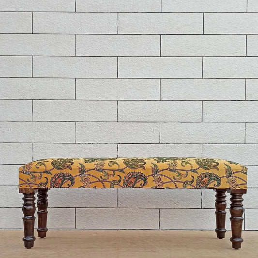 A yellow upholstered bench with a floral pattern, featuring a solid color background.