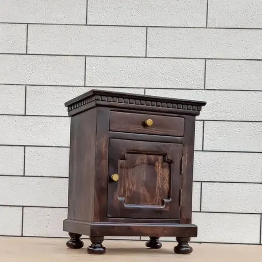 A solid wood bedside table in walnut finish with a drawer and a door, featuring turned-round legs and gold-colored hardware.