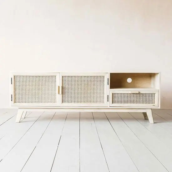 A white Atlanta TV Cabinet with cane details, featuring two doors and one drawer, placed on a white wooden floor against a plain wall.