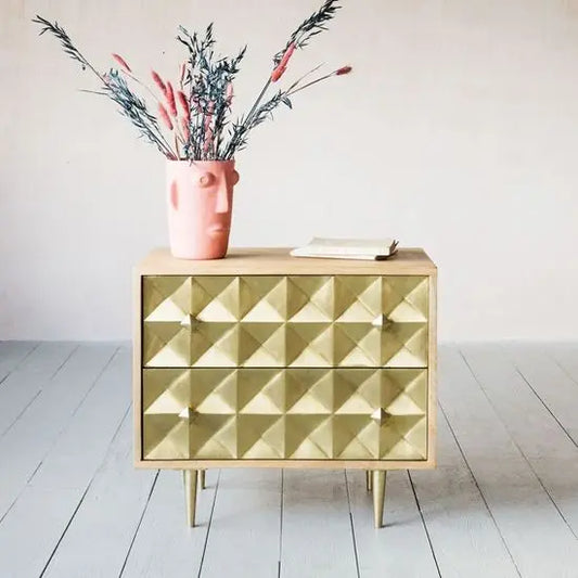 A modern Venice Bedside table with geometric hand carving and metallic accents, featuring two drawers and standing on metal legs.