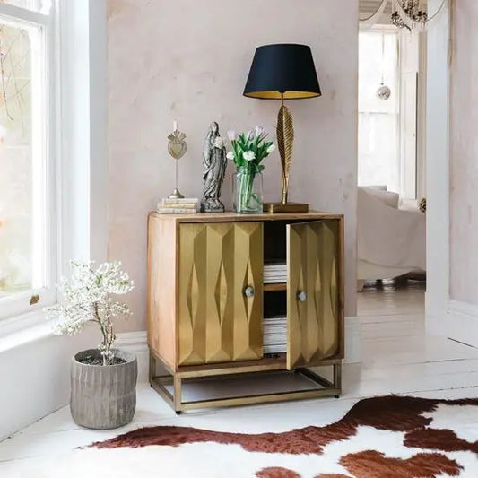 A brass sideboard with a geometric pattern on the front. placed in a room with a light pink wall and a brown rug.