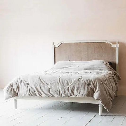 A white upholstered bed frame with wooden structure, positioned against a neutral background with a light-colored bedsheet and no other furniture.