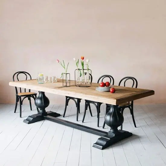 A sturdy mango wood dining table with solid turned legs, featuring a natural wood finish and a black metal base.