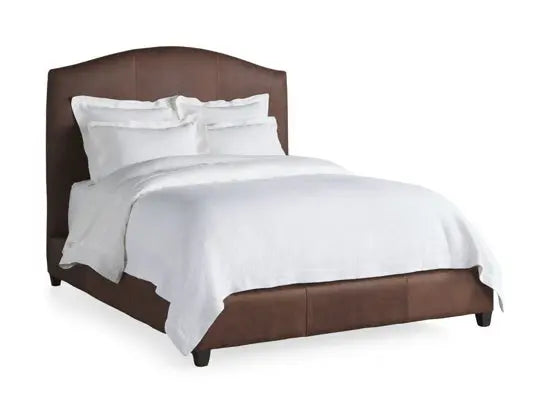 A bed with a brown headboard and white bedding, with a decorative white blanket on the bed.