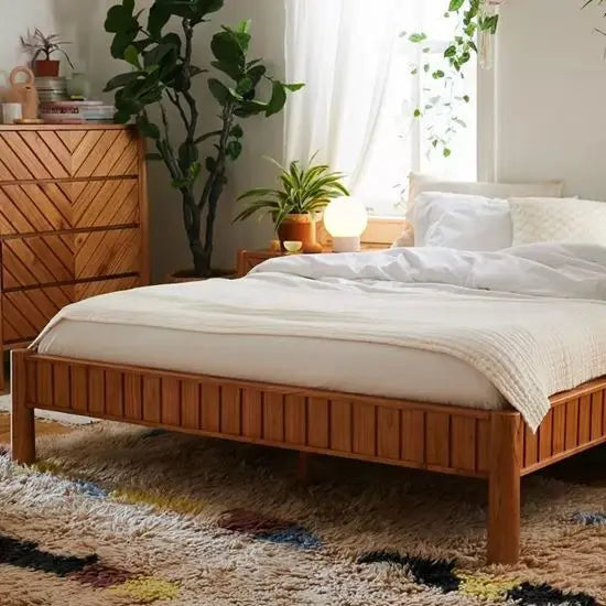 A wooden daybed with a natural finish, featured in a room setting with bedding and side tables.