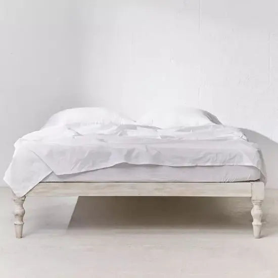 A white twin-sized bed with turned legs made of mango wood, displayed in a room setting with a white bedsheet and no pillows.