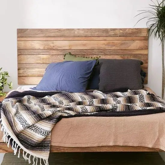 A wooden headboard with a solid pattern, featuring a rich brown color, mounted on a bed with blue and beige bedding.