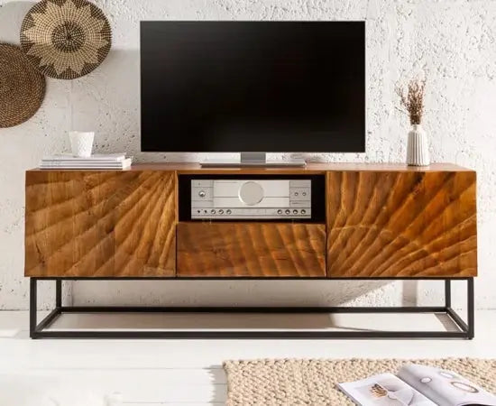 A stylish Wave TV cabinet made from high-quality mango wood with a warm honey tone finish, featuring two doors, one drawer, and an open shelf for storage. The cabinet has a sturdy metal base and is displayed in a living room setting with a flat-screen TV on top.