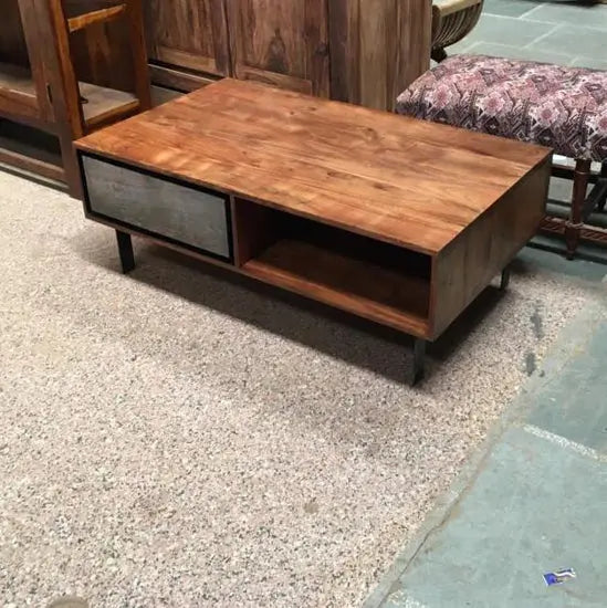 A Jarrah Coffee Table with acacia wood top, metal legs, and a natural stone drawer front, along with two open shelves.