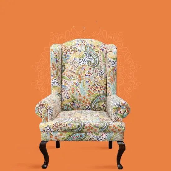 A Katha Maharaja sofa with a floral fabric design on a wing chair-style frame with wooden legs.