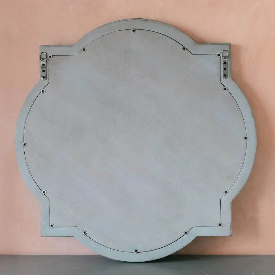 A round wall mirror with a scalloped, quatrefoil-like border, shown from the back.