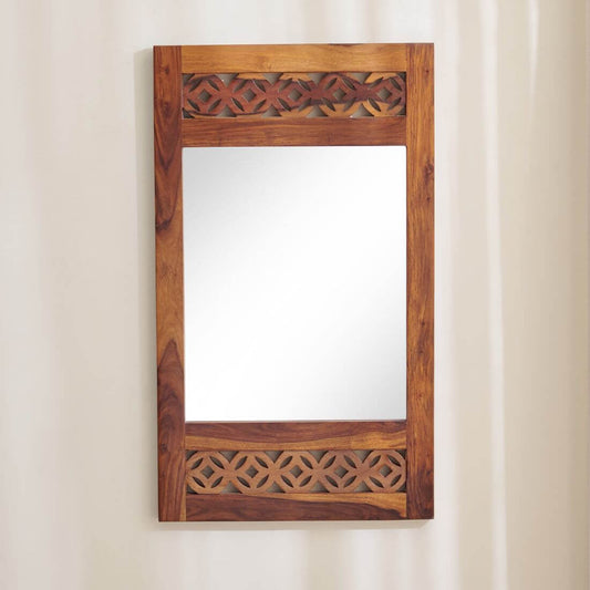 A rectangular wooden wall mirror with an ornate carved frame, featuring geometric cutout patterns at the top and bottom, mounted on a wall.